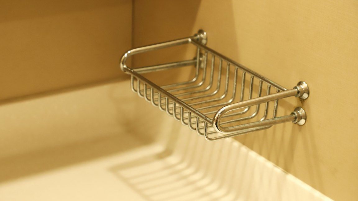 Un panier en fil de métal chromé fixé à un mur beige, au-dessus du bord d’une baignoire.